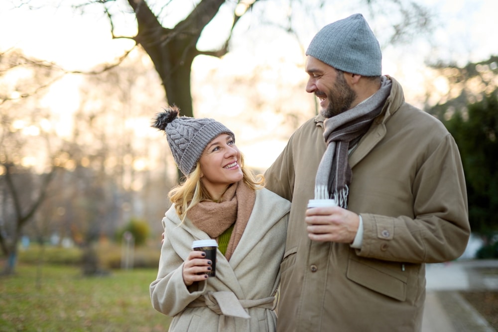 A happy couple enjoying a hot drink while taking a walk during a romantic New Hampshire getaway.