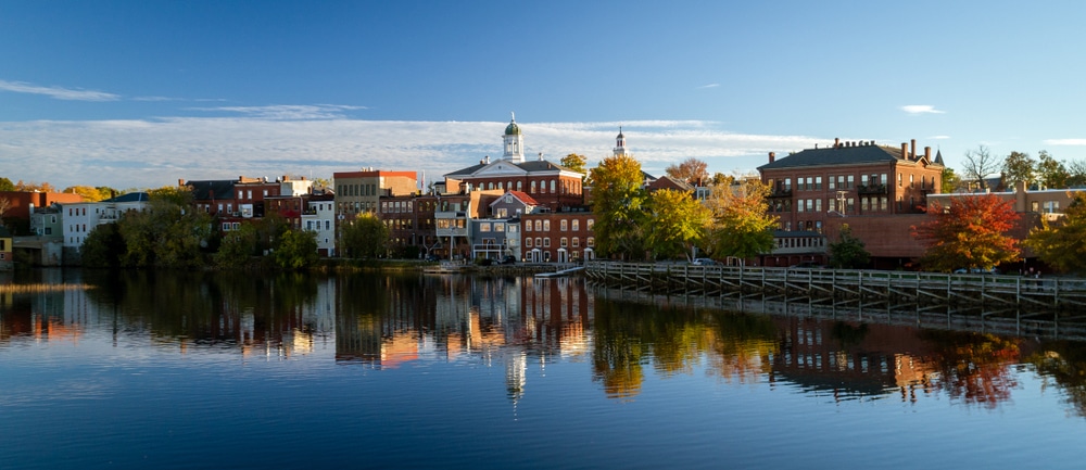 The Best Romantic New Hampshire Getaways 4 Explore Exeter, one of the most romantic New Hampshire getaways. Waterfront of Exeter lined with trees and buildings.